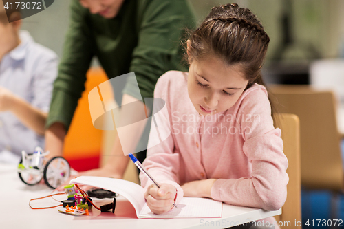 Image of happy girl writing to notebook at robotics school