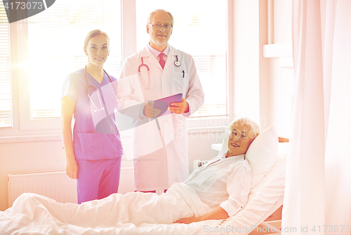 Image of doctor and nurse visiting senior woman at hospital