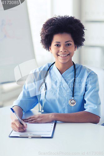 Image of happy female doctor or nurse writing to clipboard