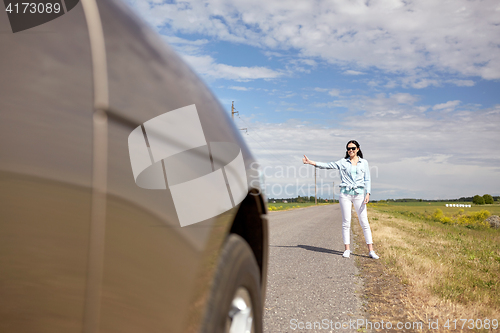 Image of woman hitchhiking and stopping car with thumbs up