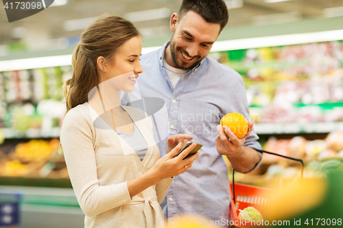 Image of couple with smartphone buying oranges at grocery