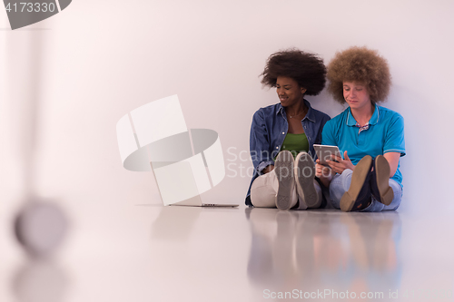 Image of multiethnic couple sitting on the floor with a laptop and tablet