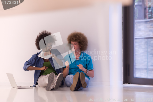 Image of multiethnic couple sitting on the floor with a laptop and tablet