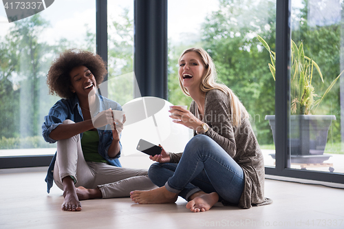 Image of multiethnic women sit on the floor and drinking coffee