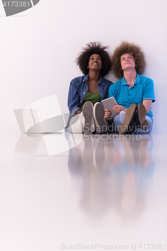 Image of multiethnic couple sitting on the floor with a laptop and tablet
