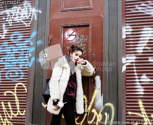 Image of young pretty stylish teenage girl outside at city wall with graf