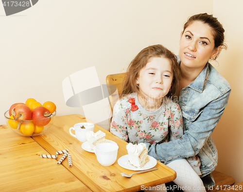 Image of young mother with daughter on kitchen drinking tea together hugging eating celebration cake on birthday party 