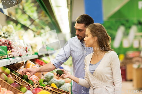 Image of happy couple buying avocado at grocery store