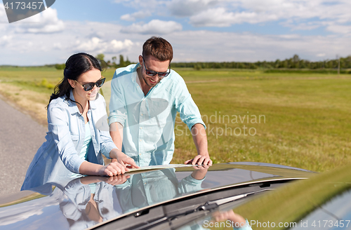 Image of happy man and woman with road map on car hood