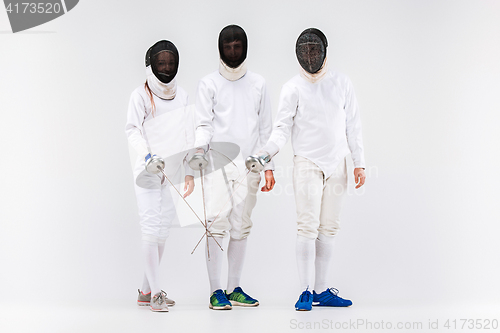Image of The two men and woman wearing fencing suit with sword against gray