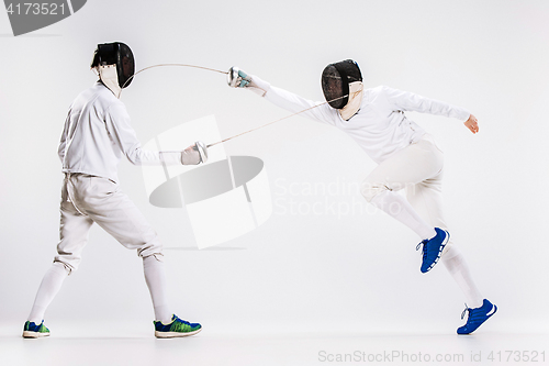 Image of The two men wearing fencing suit practicing with sword against gray