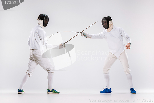 Image of The two men wearing fencing suit practicing with sword against gray