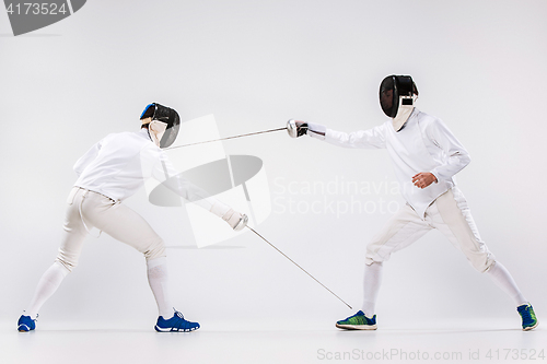 Image of The two men wearing fencing suit practicing with sword against gray