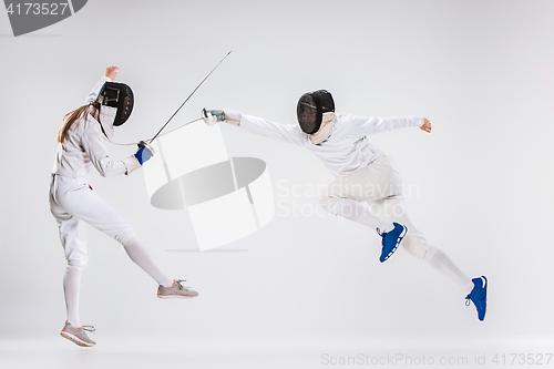 Image of The men and woman wearing fencing suit practicing with sword against gray