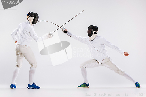 Image of The two men wearing fencing suit practicing with sword against gray