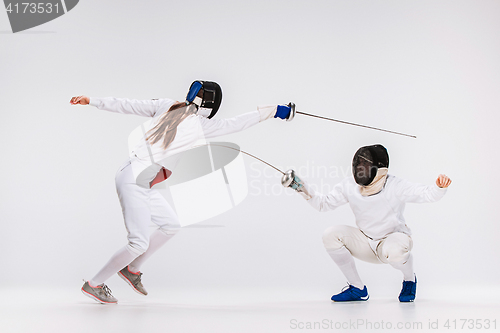 Image of The men and woman wearing fencing suit practicing with sword against gray