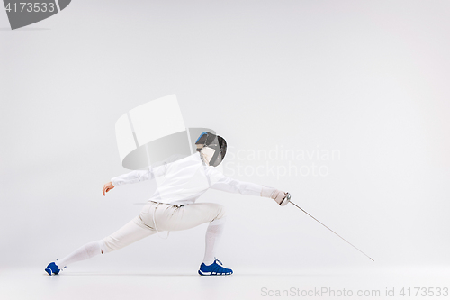 Image of Man wearing fencing suit practicing with sword against gray