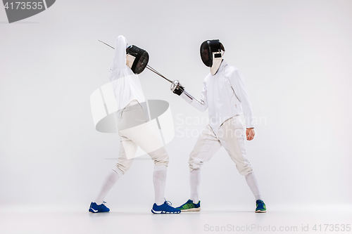 Image of The two men wearing fencing suit practicing with sword against gray