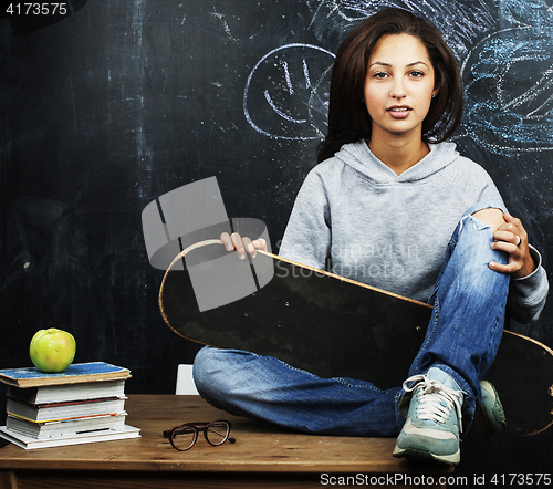 Image of young cute teenage girl in classroom at blackboard seating on ta