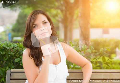 Image of Young Adult Female Student with Pencil on Bench Outdoors