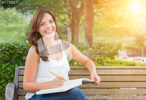 Image of Young Adult Female Student with Pencil on Bench Outdoors