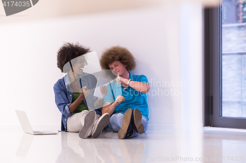 Image of multiethnic couple sitting on the floor with a laptop and tablet