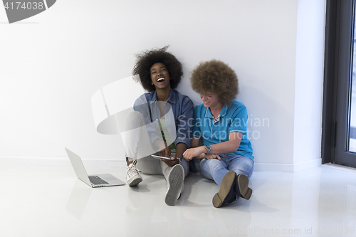 Image of multiethnic couple sitting on the floor with a laptop and tablet