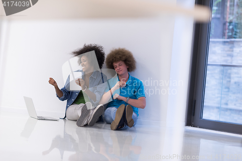 Image of multiethnic couple sitting on the floor with a laptop and tablet