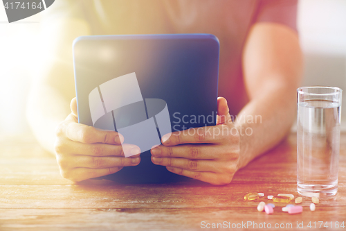 Image of close up of hands with tablet pc, pills and water