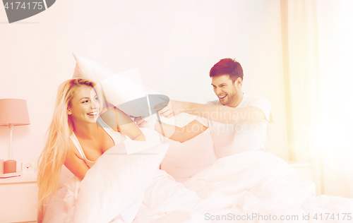 Image of happy couple having pillow fight in bed at home