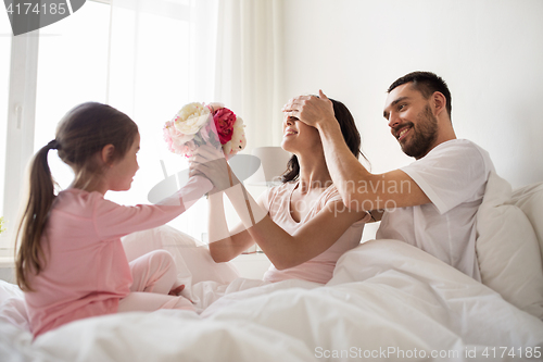 Image of happy girl giving flowers to mother in bed at home