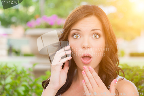 Image of Shocked Young Adult Female Talking on Cell Phone Outdoors