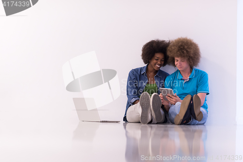 Image of multiethnic couple sitting on the floor with a laptop and tablet