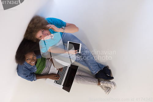 Image of multiethnic couple sitting on the floor with a laptop and tablet