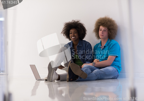 Image of multiethnic couple sitting on the floor with a laptop and tablet