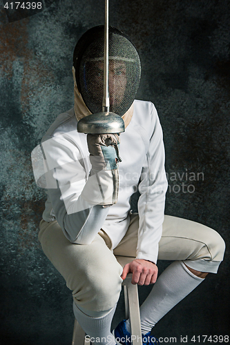 Image of The man wearing fencing suit with sword against gray