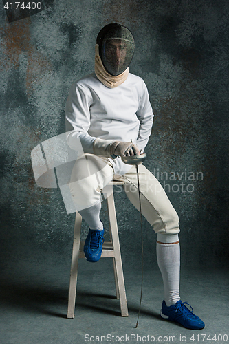 Image of The man wearing fencing suit with sword against gray