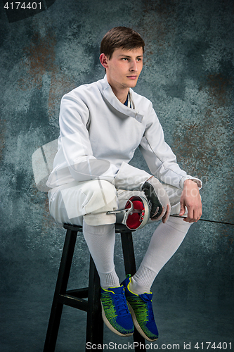 Image of The man wearing fencing suit with sword against gray