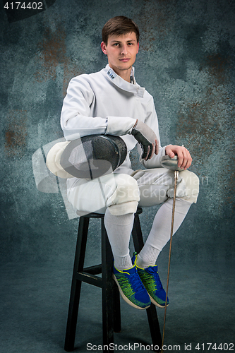 Image of The man wearing fencing suit with sword against gray