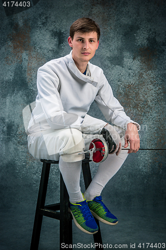 Image of The man wearing fencing suit with sword against gray