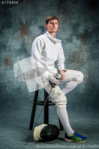 Image of The man wearing fencing suit with sword against gray