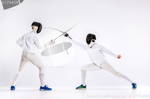 Image of The two men wearing fencing suit practicing with sword against gray