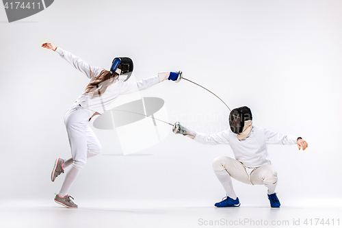 Image of The woman and man wearing fencing suit practicing with sword against gray