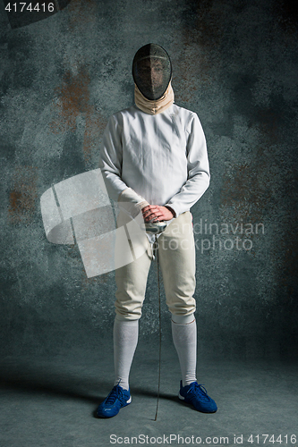 Image of The man wearing fencing suit with sword against gray