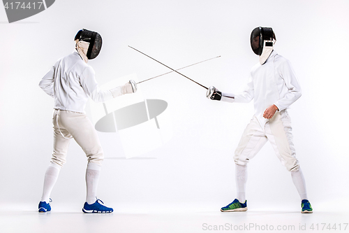 Image of The two men wearing fencing suit practicing with sword against gray