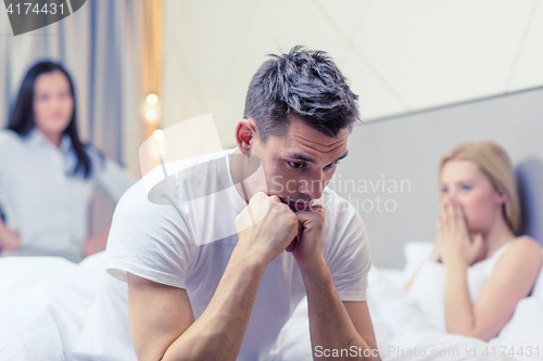 Image of man sitting on the bed with two women on the back