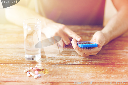 Image of close up of hands with smartphone, pills and water