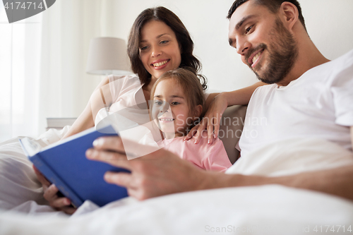 Image of happy family reading book in bed at home