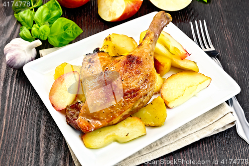 Image of Duck leg with apple and basil in plate on dark board