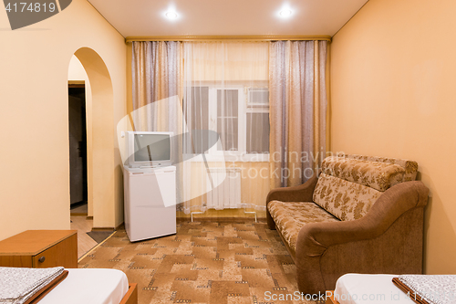 Image of The interior of a small room with sofa bed and two single beds, window, TV and fridge